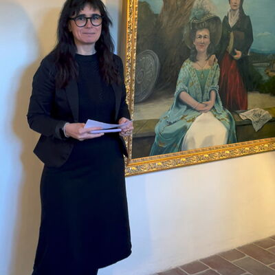 Roxana Panetta steht vor einem großen Gemälde und stellt in einem kurzweiligen Vortrag ihre Arbeit für die Sichtbarkeit von Frauen vor