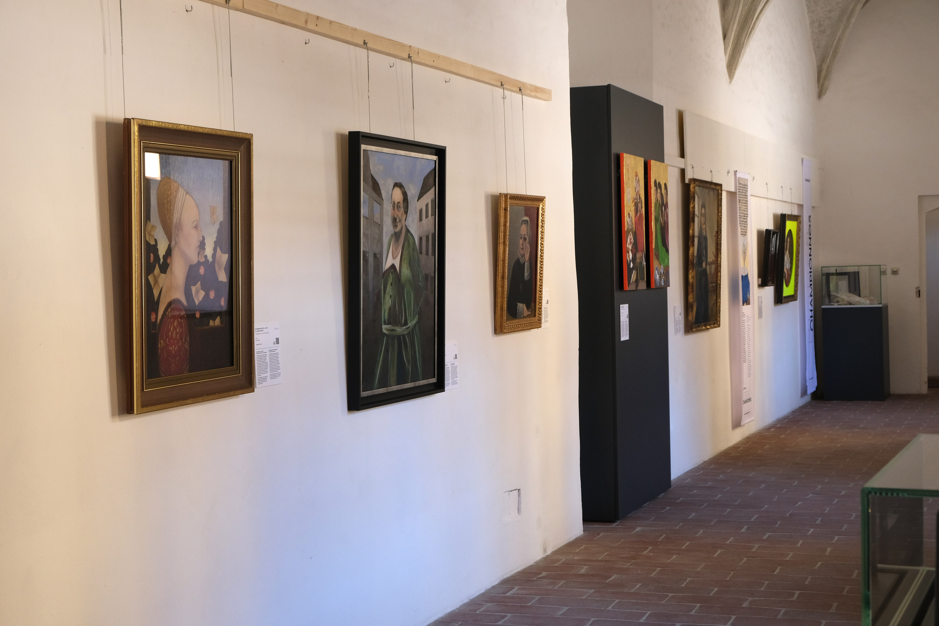 Foto des Kapellgangs, eines langen Flurs, mit Fenstern auf einer Seite und Frauen-Portraits in alten wertvollen Holzrahmen auf der anderen Seite